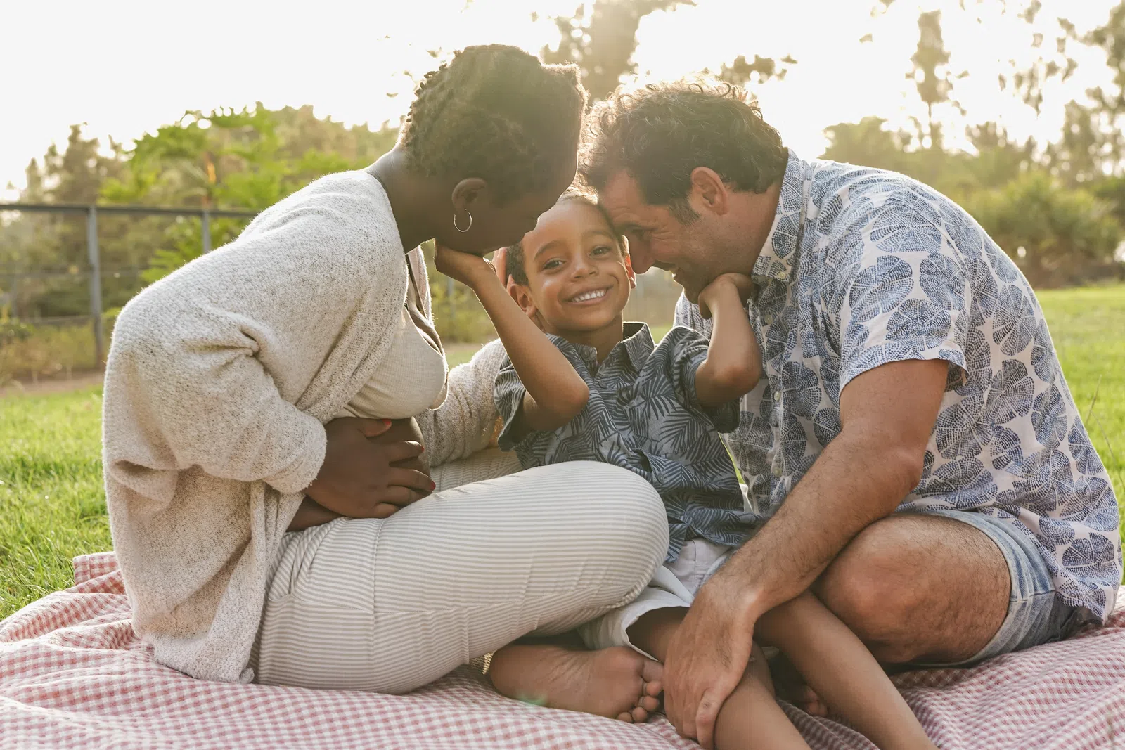 Happy diverse family enjoying a picnic outdoors on a blanket with loving parents and smiling child.