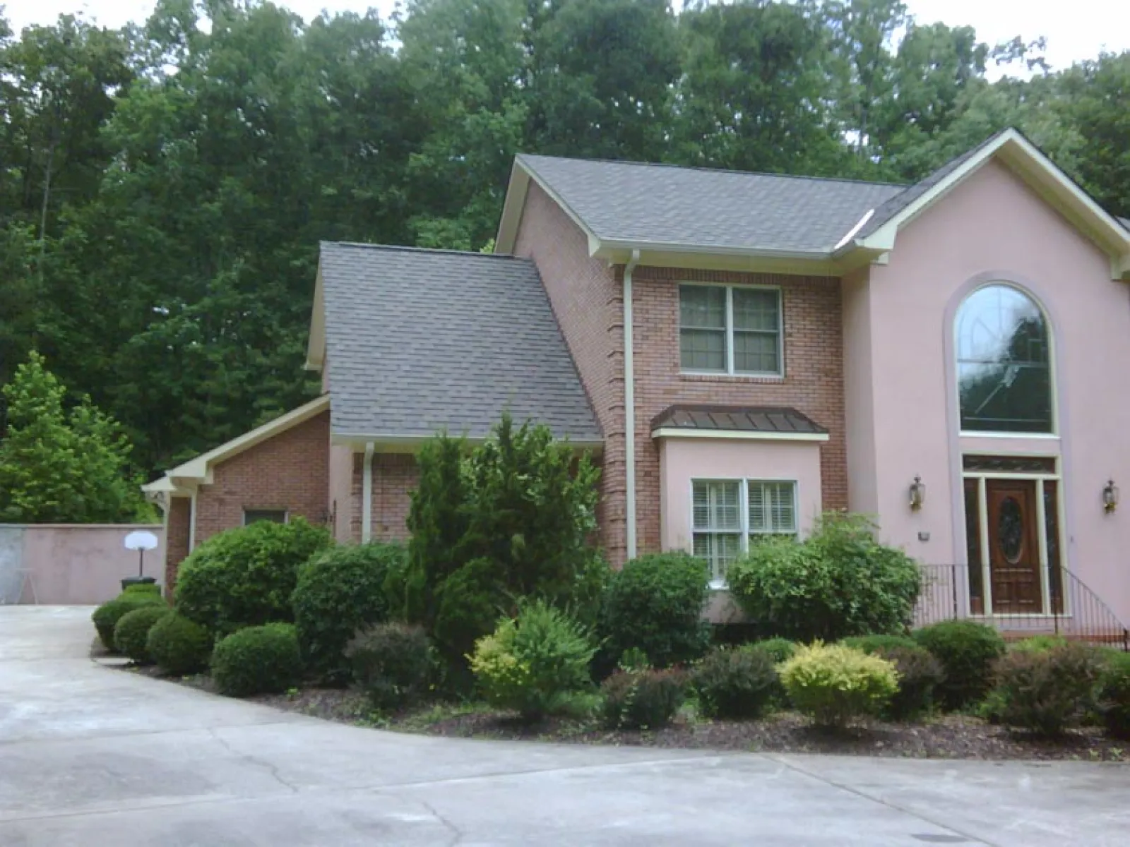 Two-story brick and stucco house with large driveway and well-maintained front yard shrubs and trees.