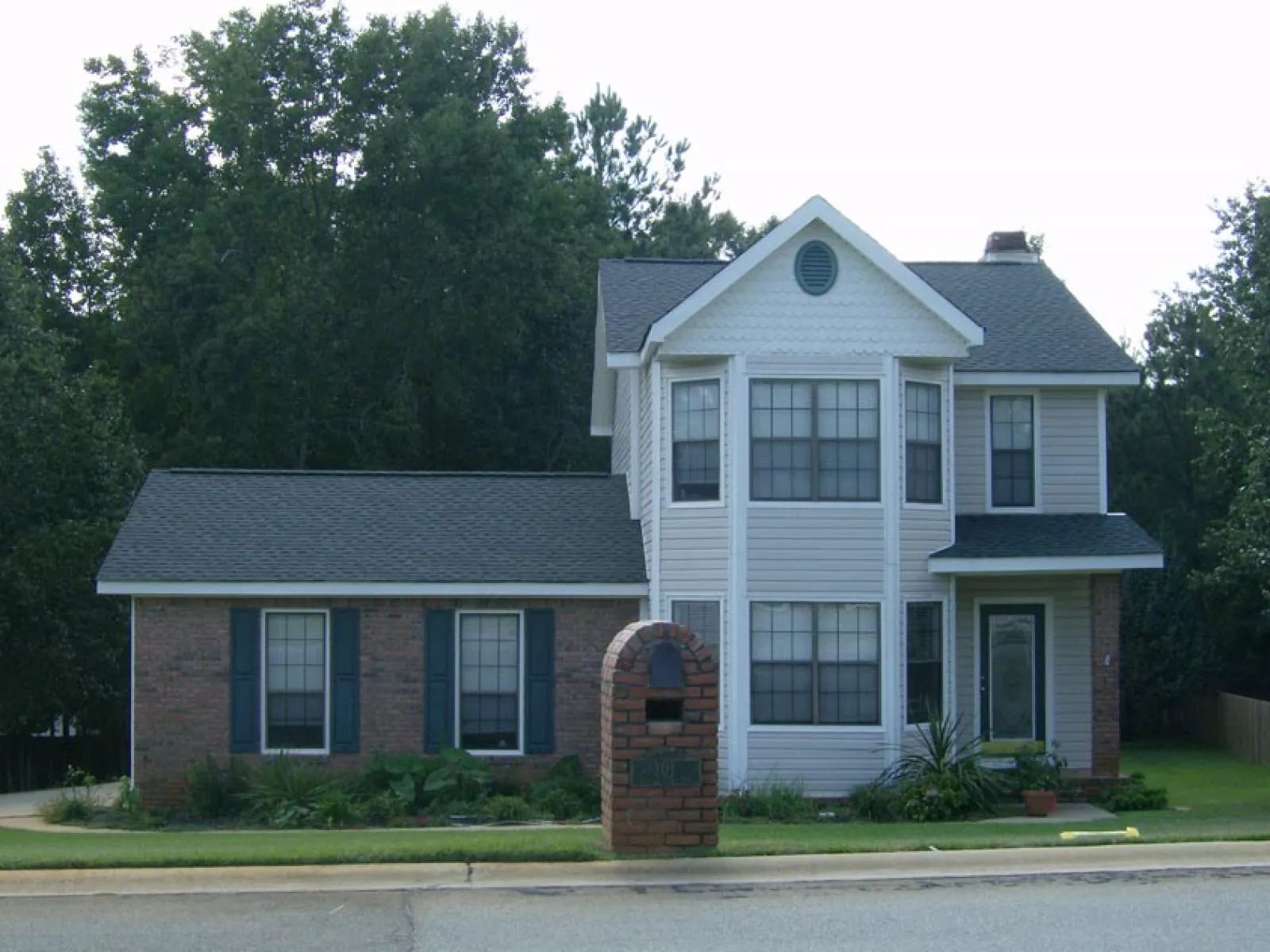 Two-story suburban house with brick and siding exterior, bay windows, and a brick mailbox by the roadside.