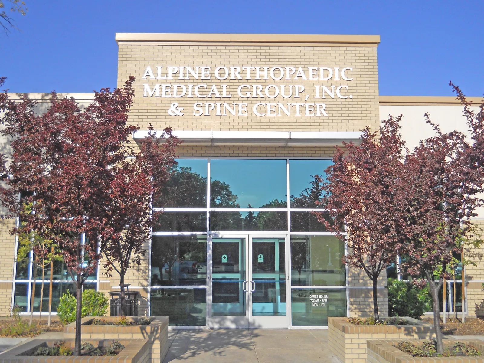 Front entrance of Alpine Orthopaedic Medical Group and Spine Center building with trees and clear sky.