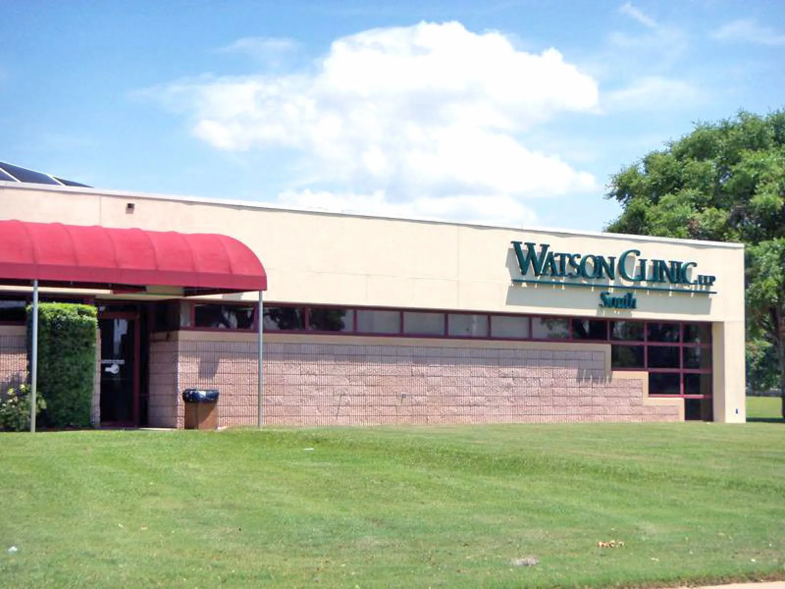 Exterior view of Watson Clinic building with red awning and green lawn under a partly cloudy sky.