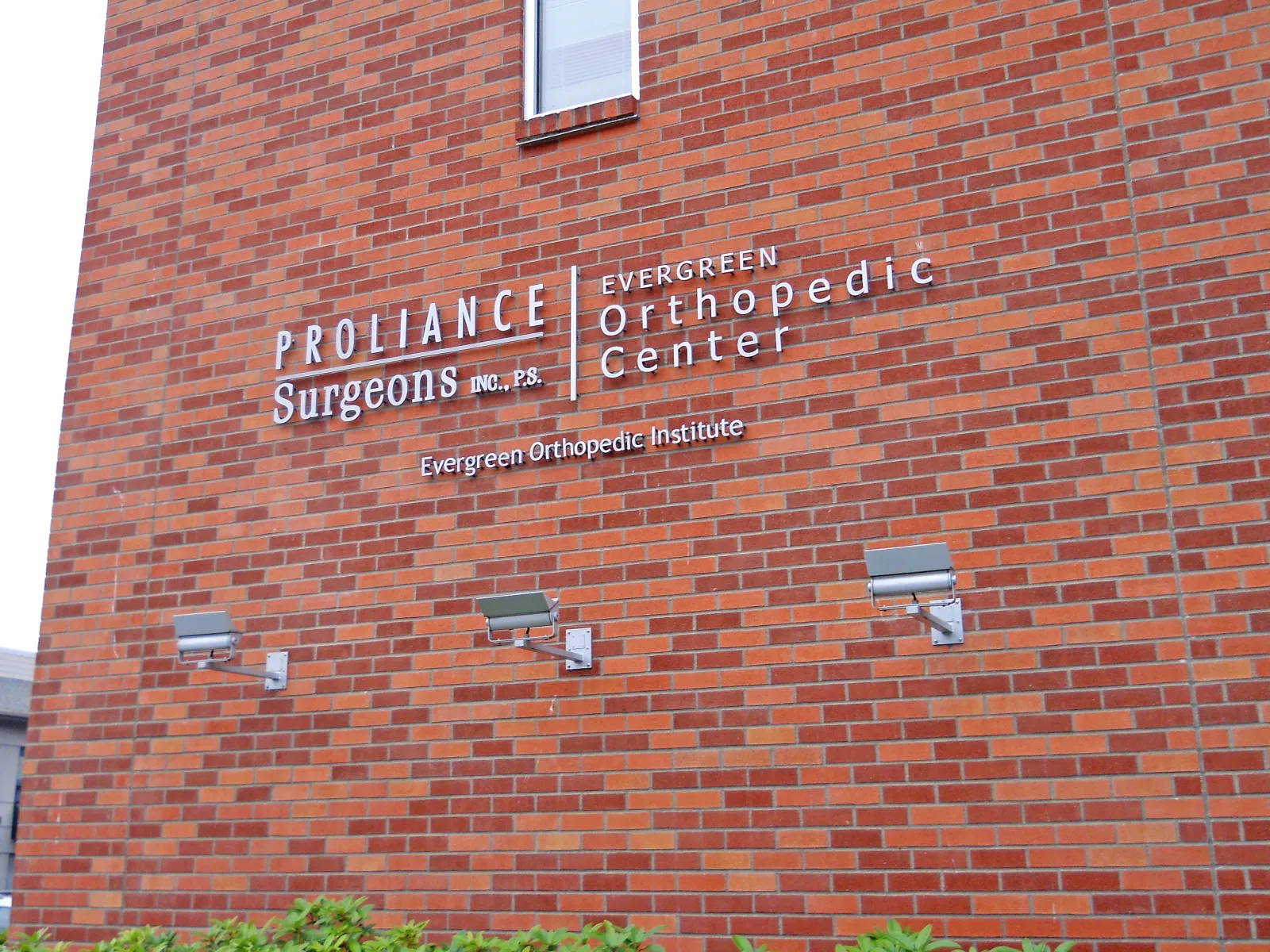 Brick building exterior displaying Proliance Surgeons and Evergreen Orthopedic Center signage with outdoor lights.