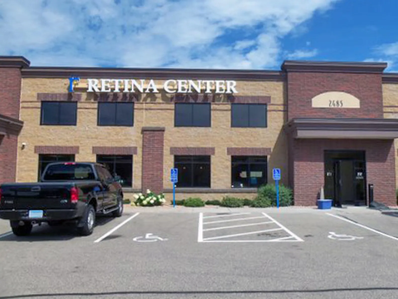 Exterior view of Retina Center medical building with parking lot and black pickup truck under blue sky