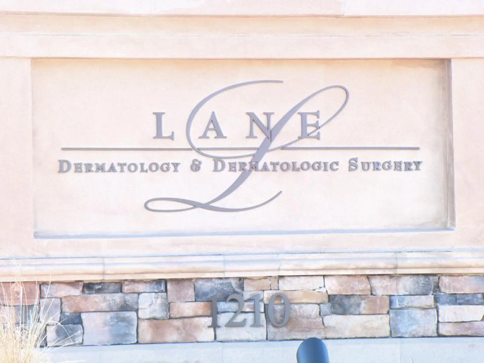 Stone sign for Lane Dermatology & Dermatologic Surgery with address number 1210 on brick base.