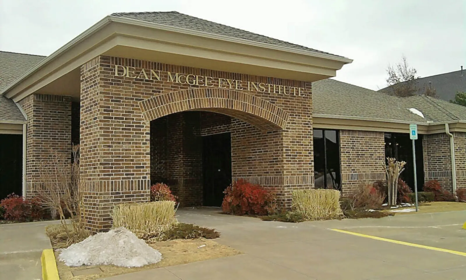 Brick building entrance of Dean McGee Eye Institute with landscaping and handicap parking sign.