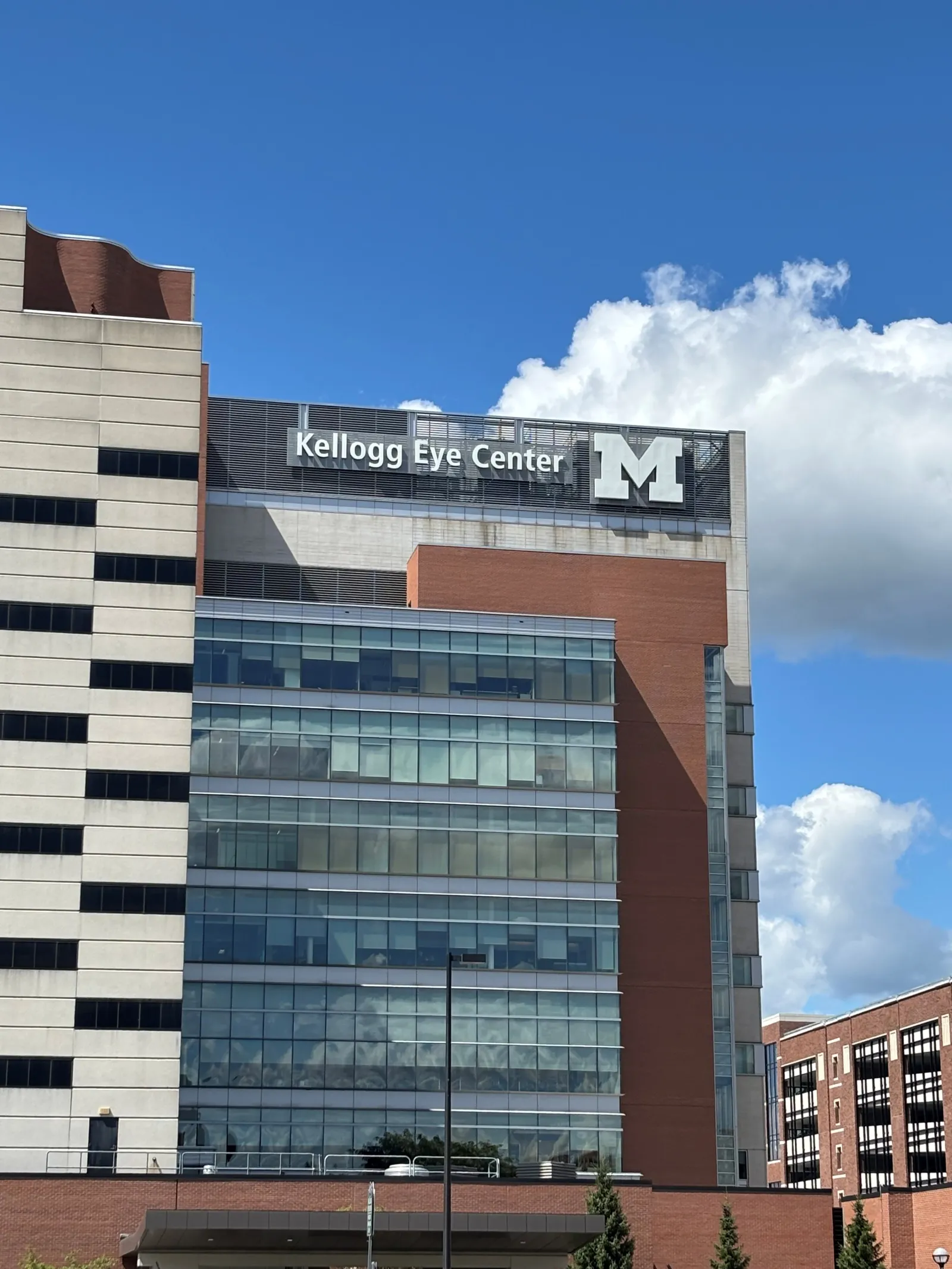 Kellogg Eye Center building with University of Michigan logo under blue sky and white clouds.