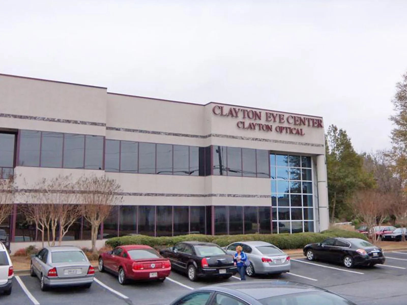 Clayton Eye Center building with parked cars and trees in front under a cloudy sky.