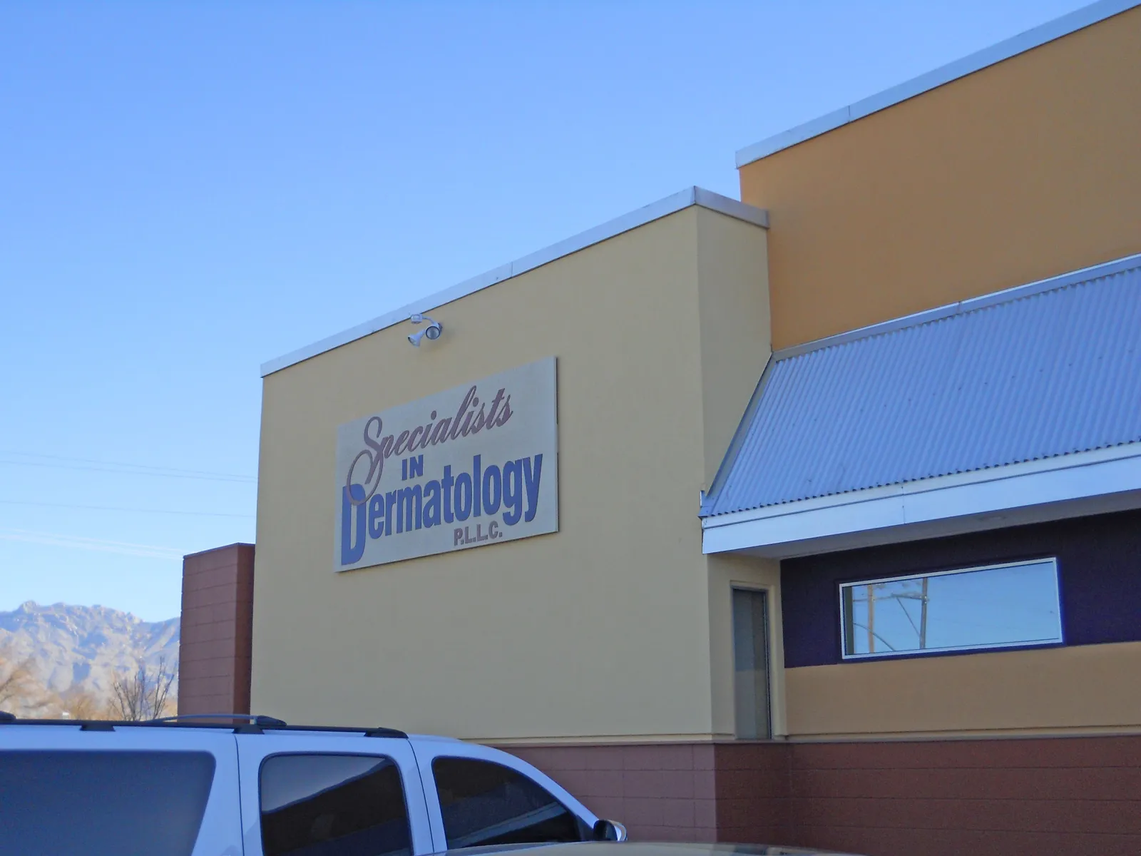 Exterior view of Specialists in Dermatology clinic with clear blue sky and mountain backdrop.