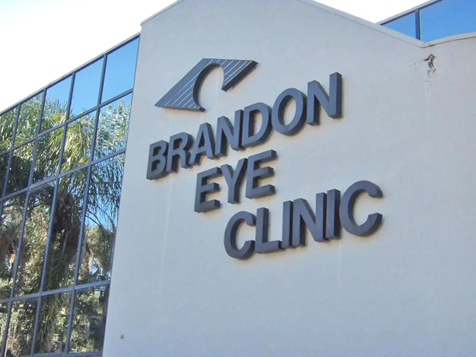 Exterior view of Brandon Eye Clinic building with reflective windows and eye logo on white wall.