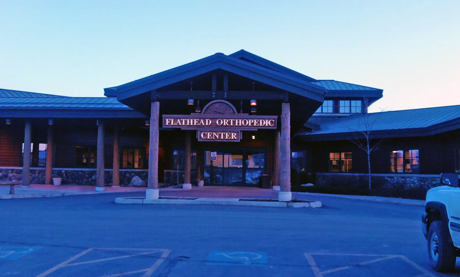 Entrance of Flathead Orthopedic Center with wooden beams and stone accents at dusk