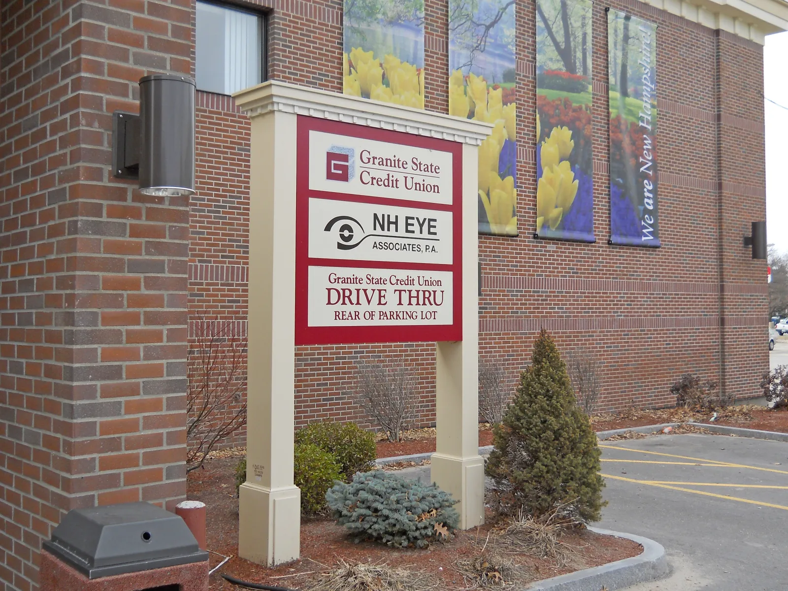 Outdoor sign for Granite State Credit Union and NH Eye Associates with drive-thru directions in parking lot area.