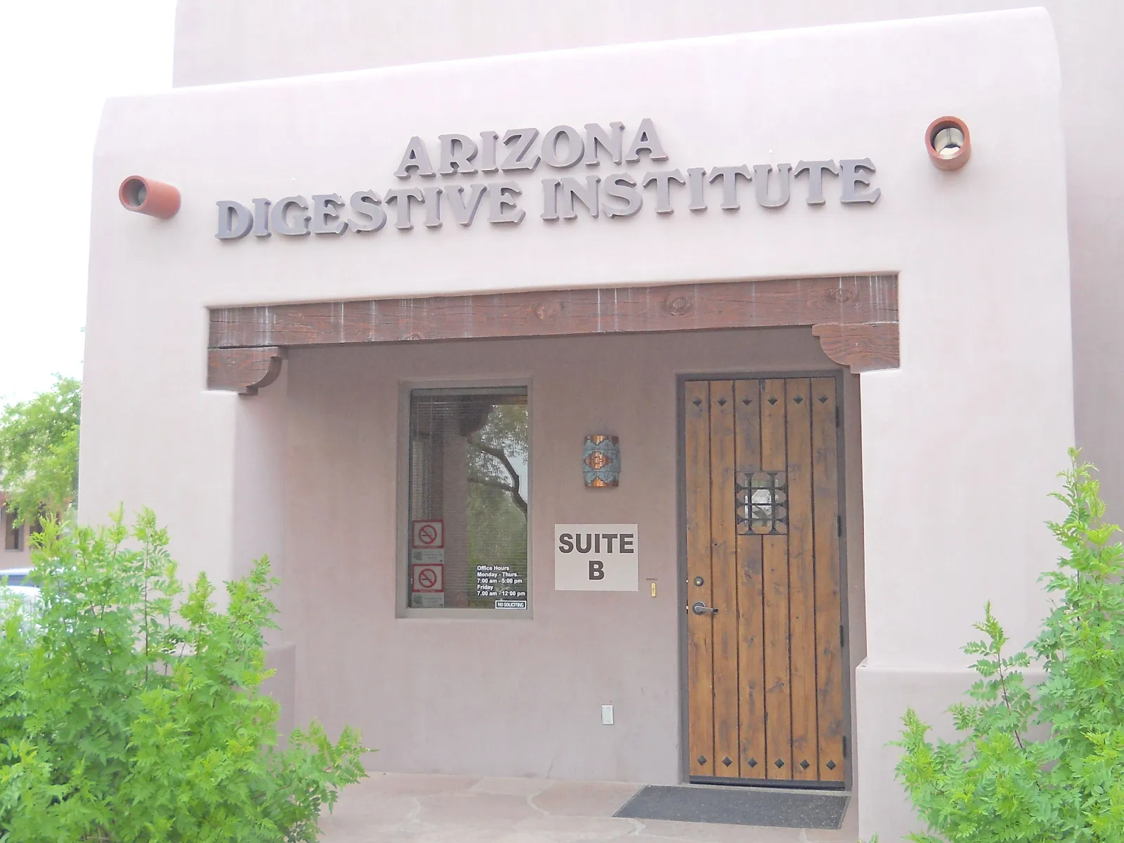 Exterior view of Arizona Digestive Institute with wooden door and window in Suite B of stucco building.