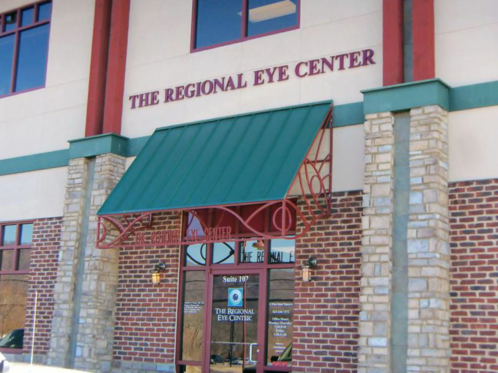 Entrance of The Regional Eye Center with green awning and stone brick facade on a sunny day