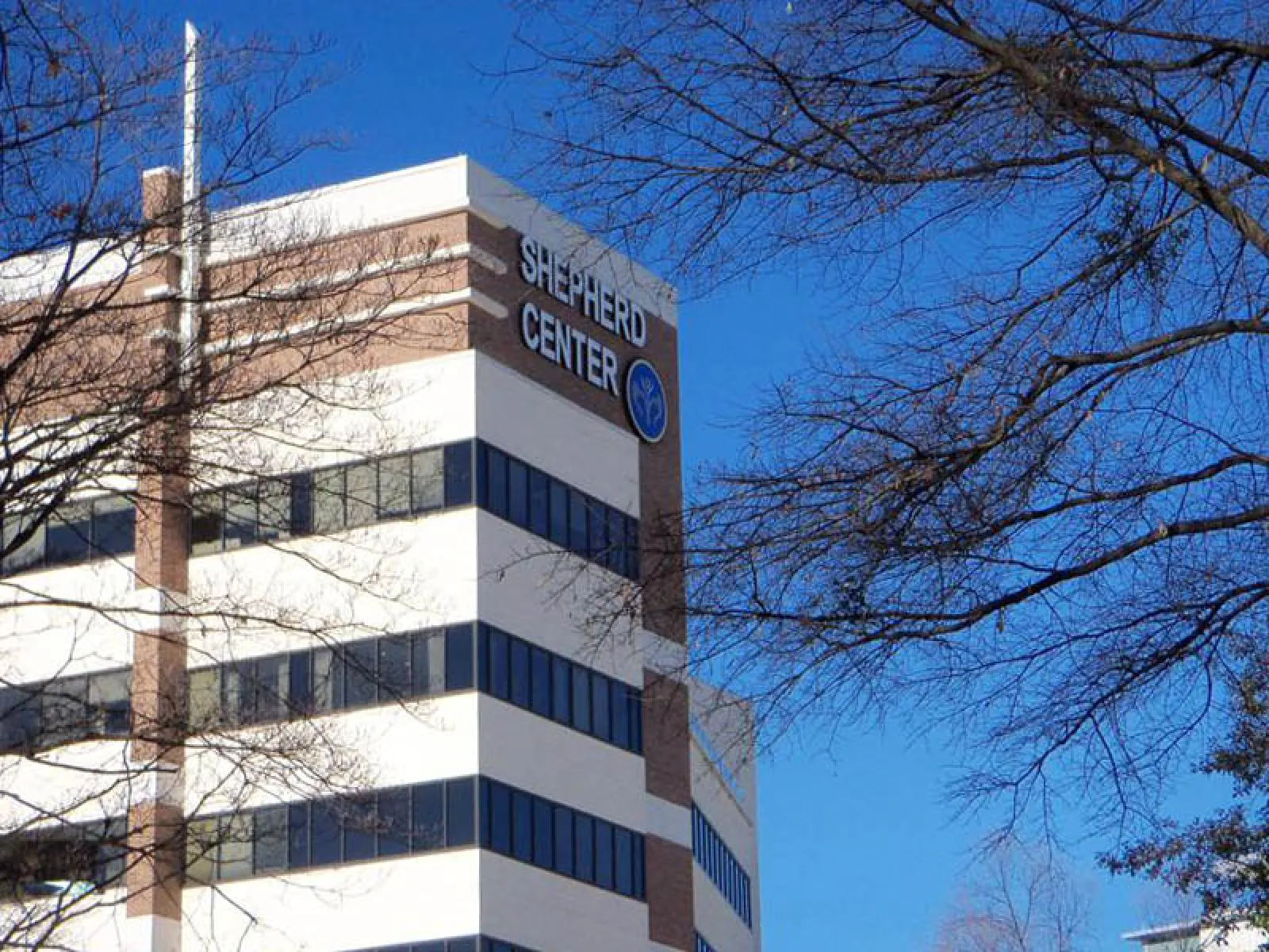 Shepherd Center medical building with blue sky and bare tree branches in foreground.