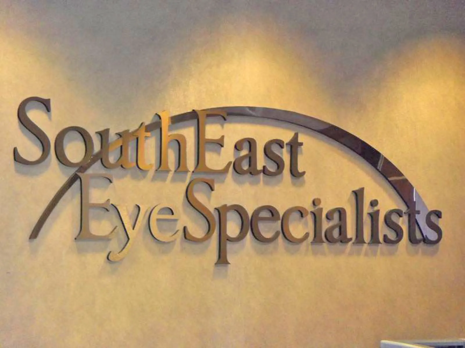 SouthEast Eye Specialists sign with arched design on beige wall under soft lighting.