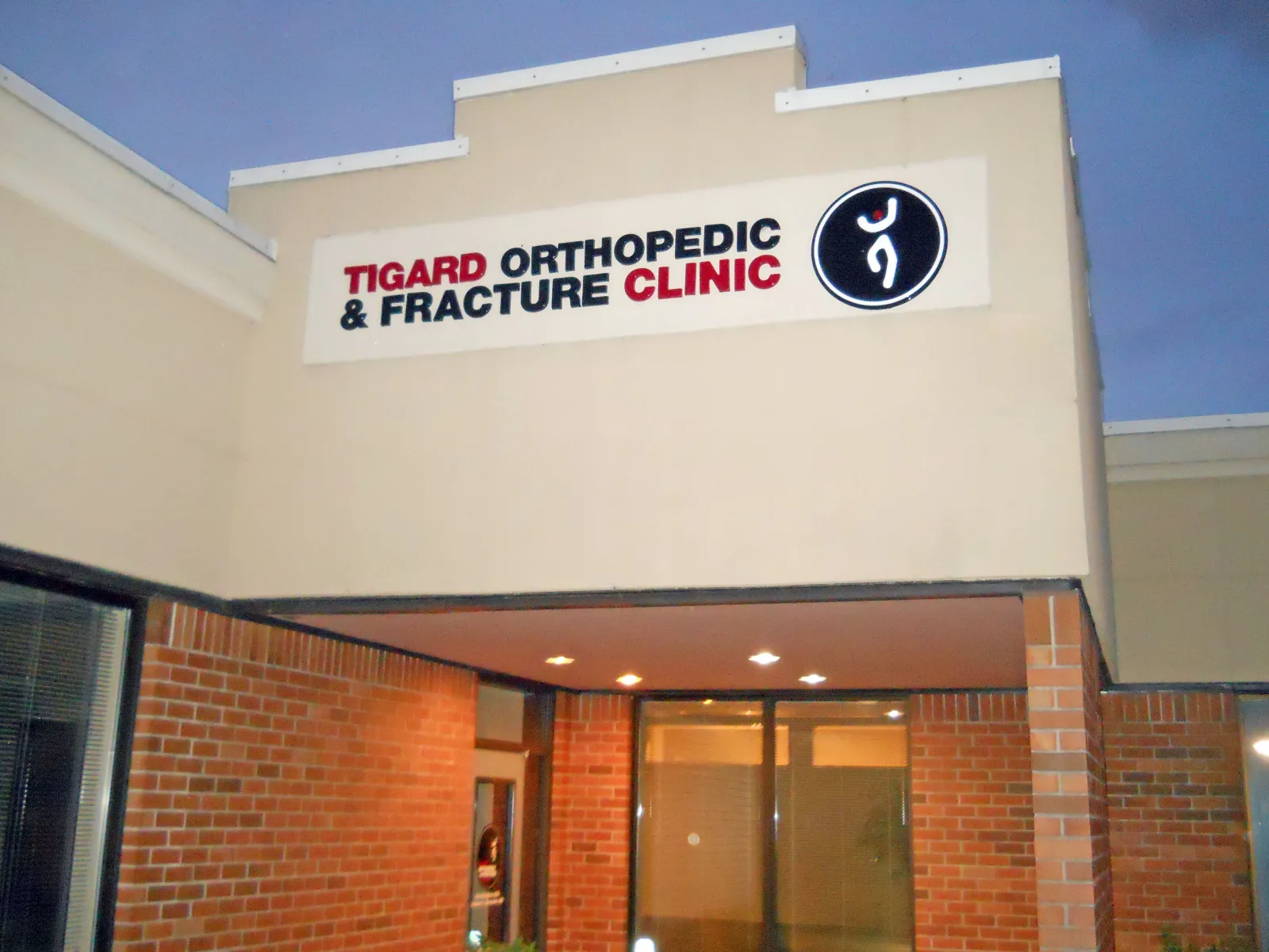 Entrance of Tigard Orthopedic and Fracture Clinic with illuminated sign and brick facade in the evening.