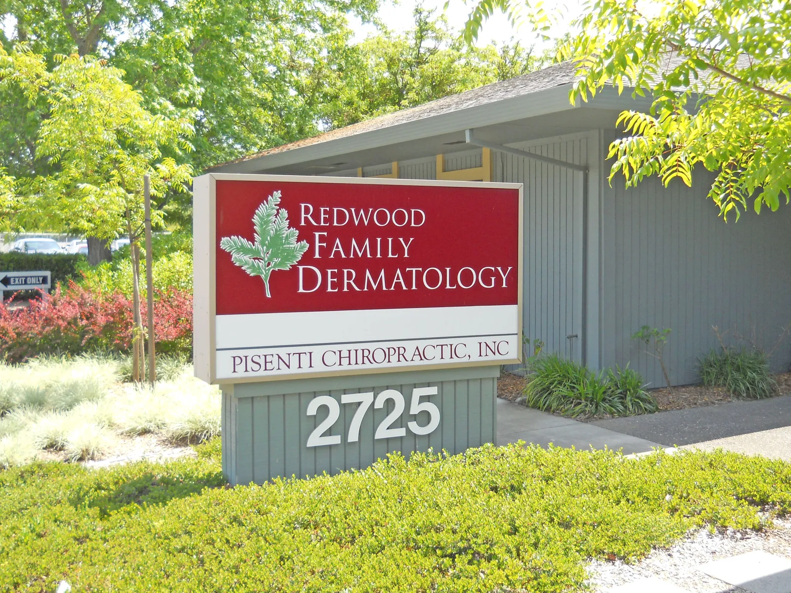 Outdoor sign for Redwood Family Dermatology and Pisenti Chiropractic with address 2725, surrounded by greenery.