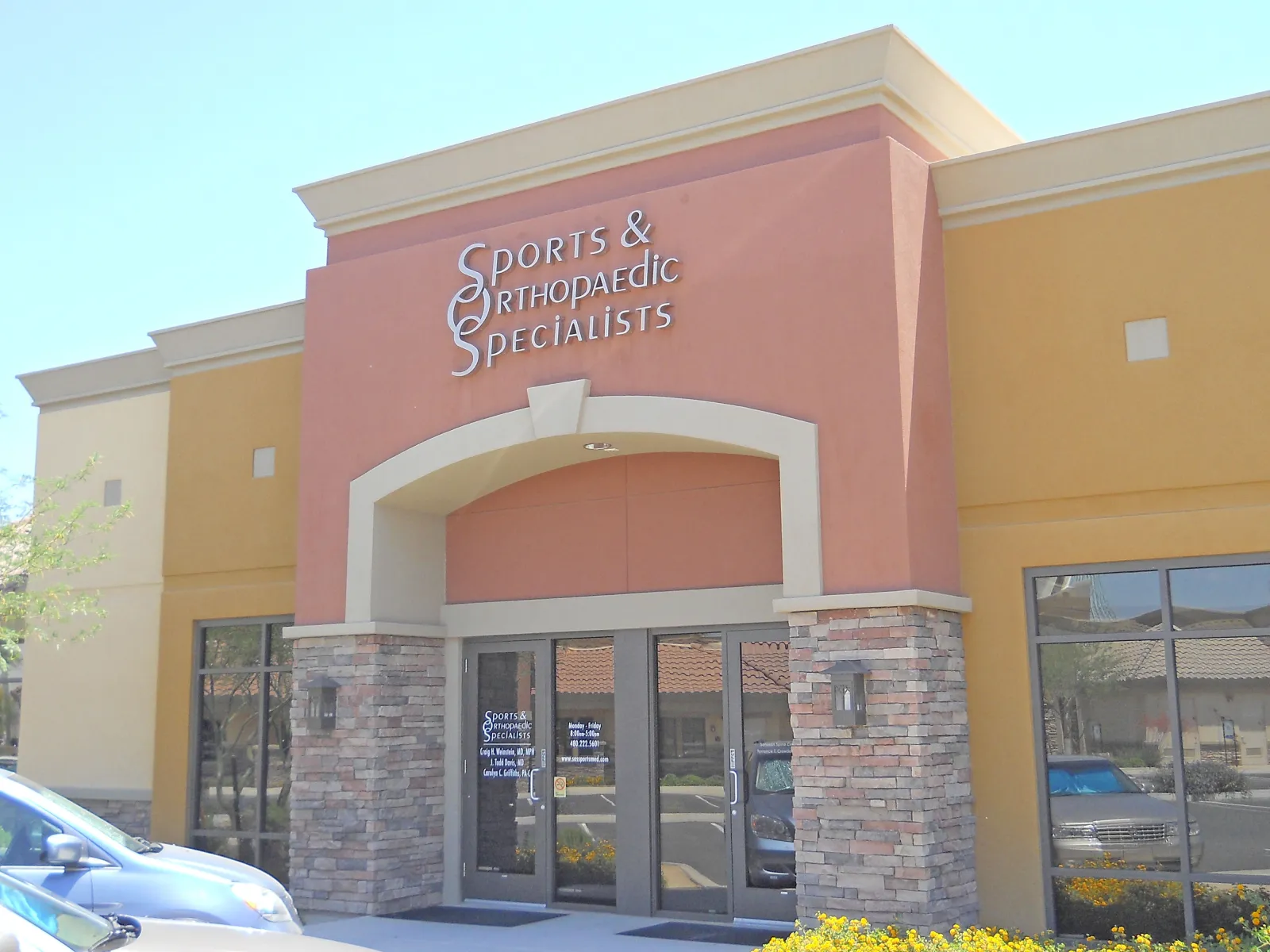 Entrance of Sports & Orthopaedic Specialists clinic with brick pillars and glass doors under clear sky