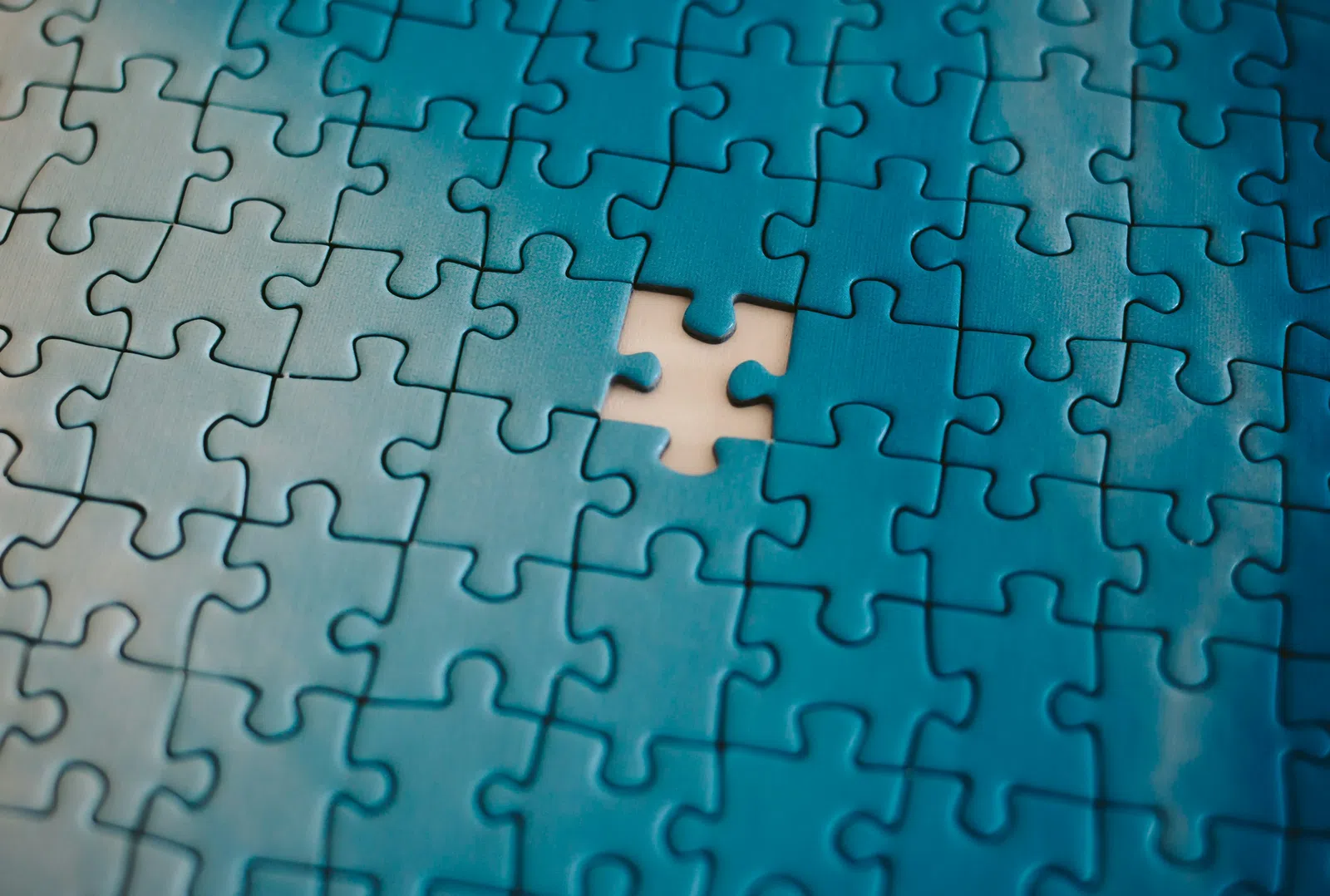 Blue jigsaw puzzle with one piece missing in the center revealing the background underneath.