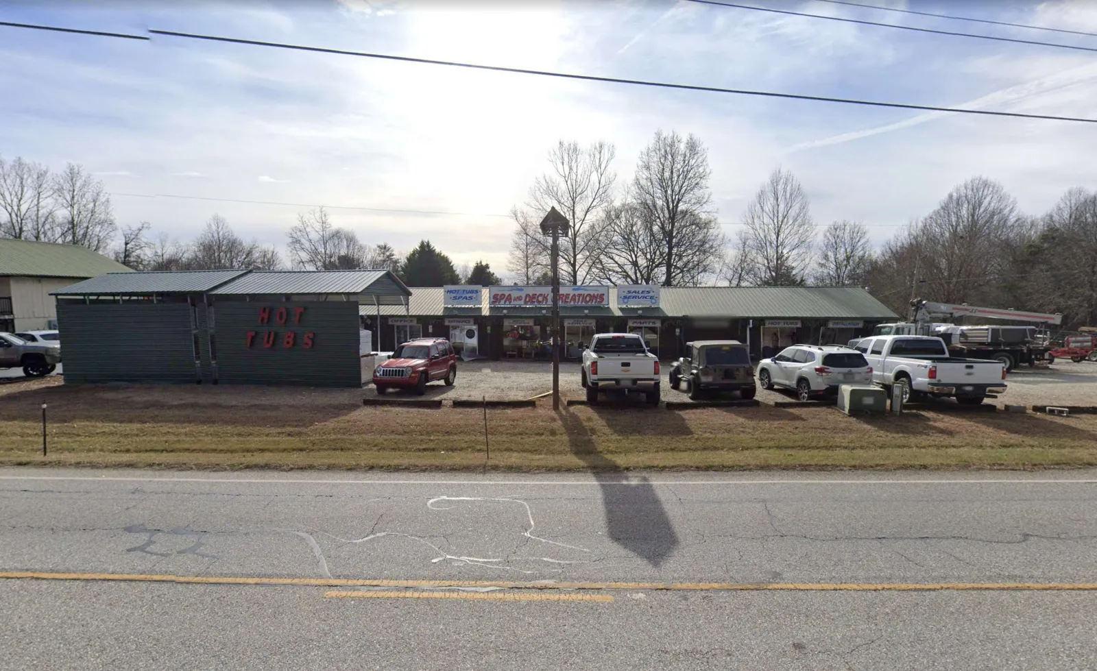Spa 'n Deck Creations store with multiple vehicles parked outside under a clear sky in a rural area.