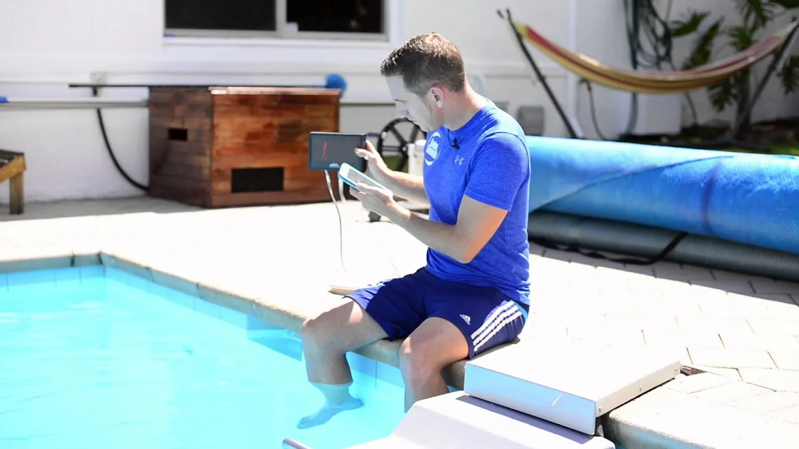 a person sitting on the side of a pool holding a device