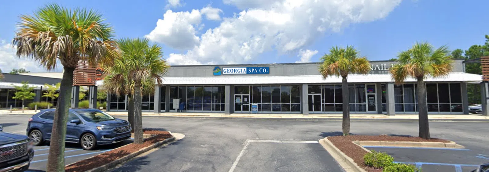 Street view of Georgia Spa Co with palm trees and parked cars in a sunny shopping plaza.