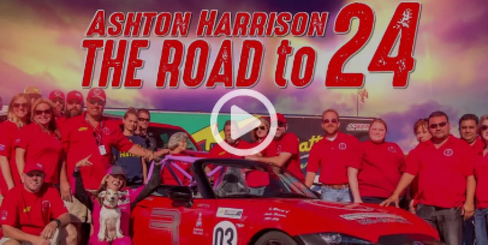 Group of people posing with a red race car under the title Ashton Harrison The Road to 24 with a sunset sky.