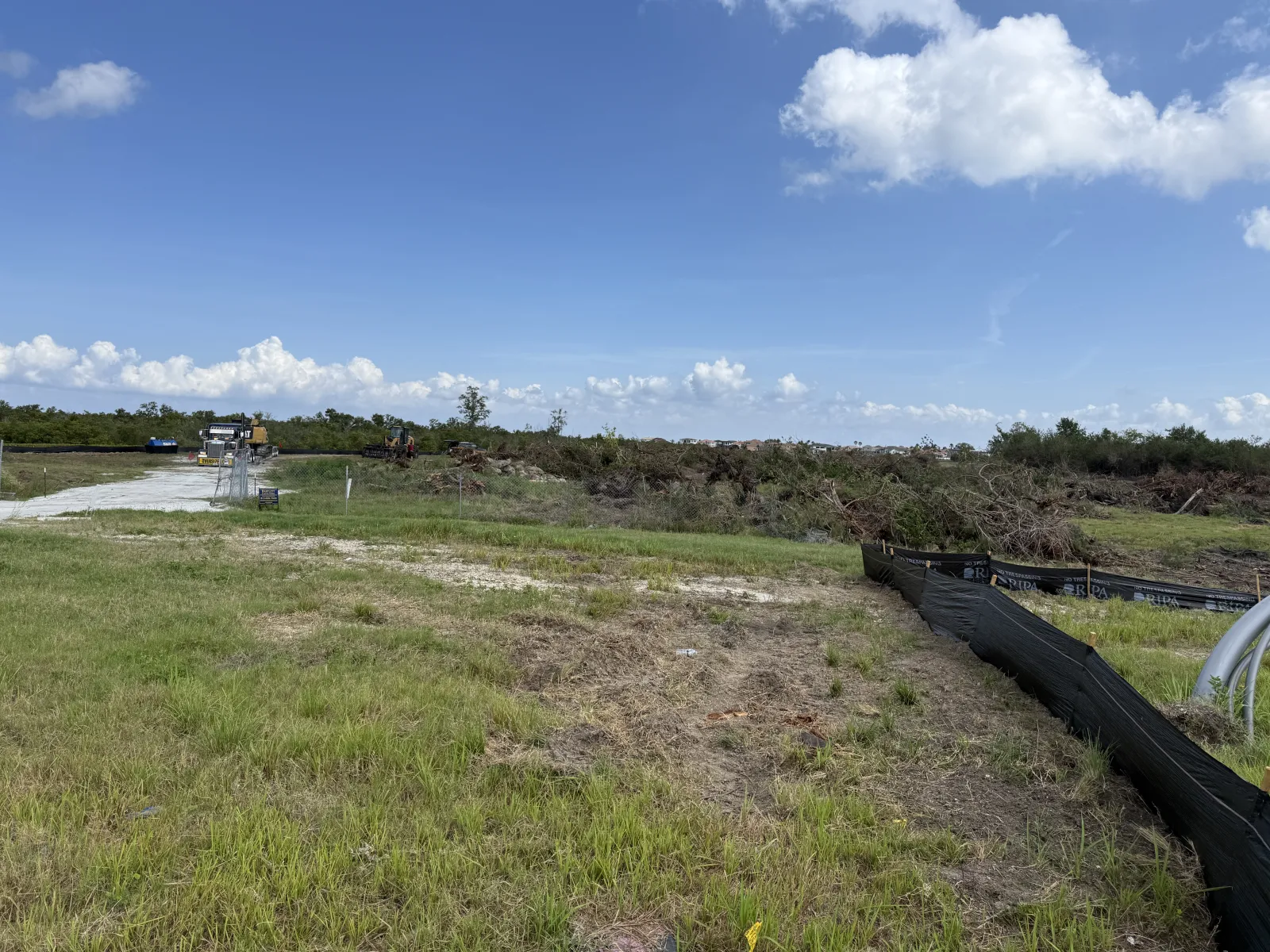 Construction site with cleared land, grassy area, machinery, and blue sky with clouds on a sunny day