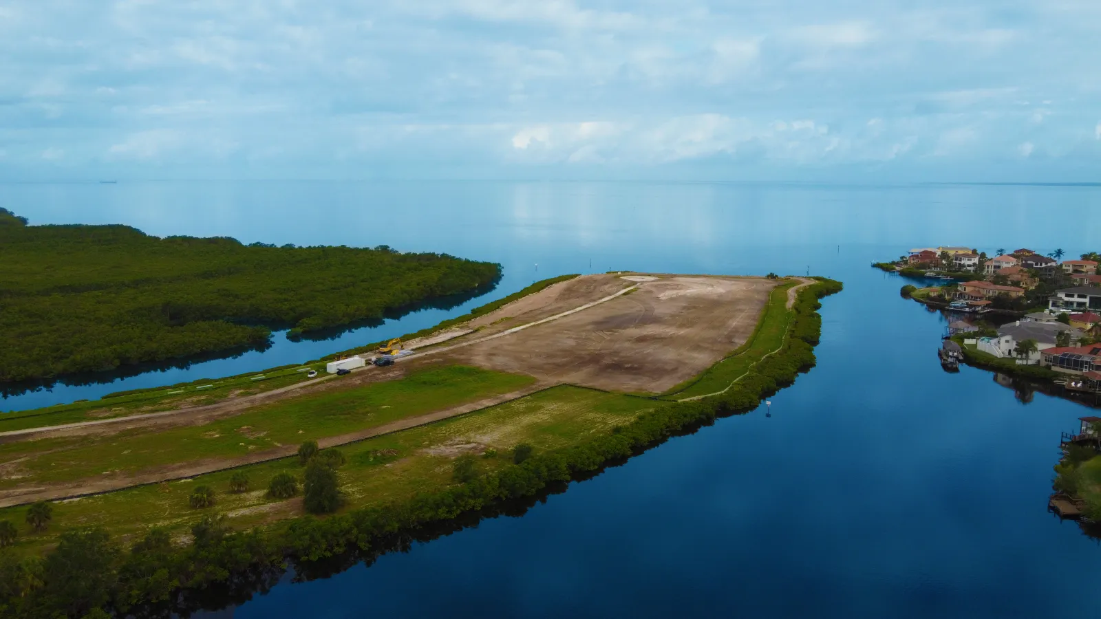 Aerial view of a waterfront development site surrounded by water channels and residential homes on a cloudy day.