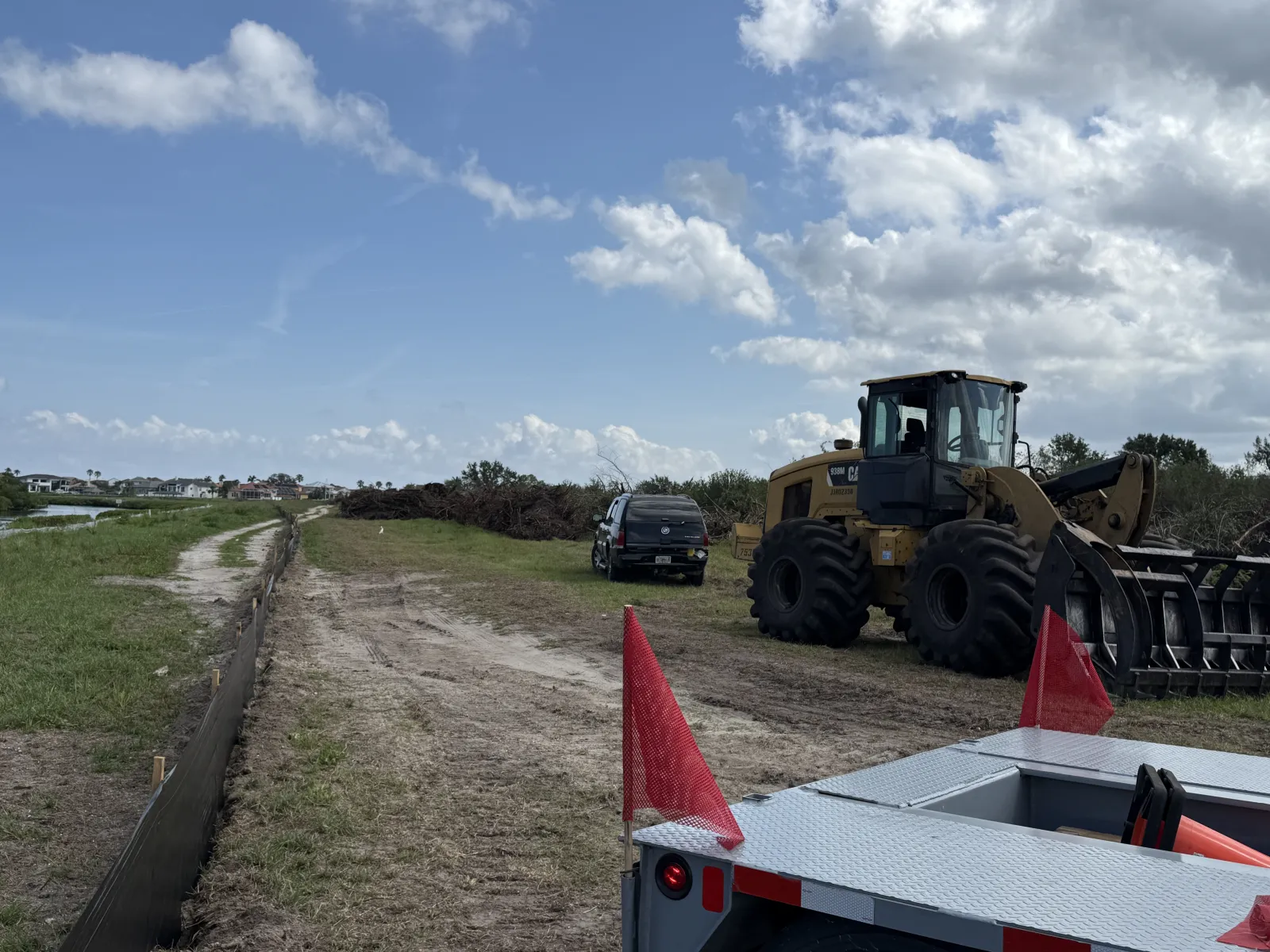Construction site with dirt road, heavy machinery, pickup truck, and red safety flags under a cloudy sky