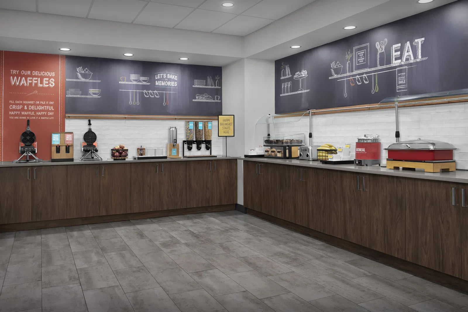 Modern breakfast buffet area with waffle makers, cereal dispensers, and wooden cabinets in a clean, spacious room.