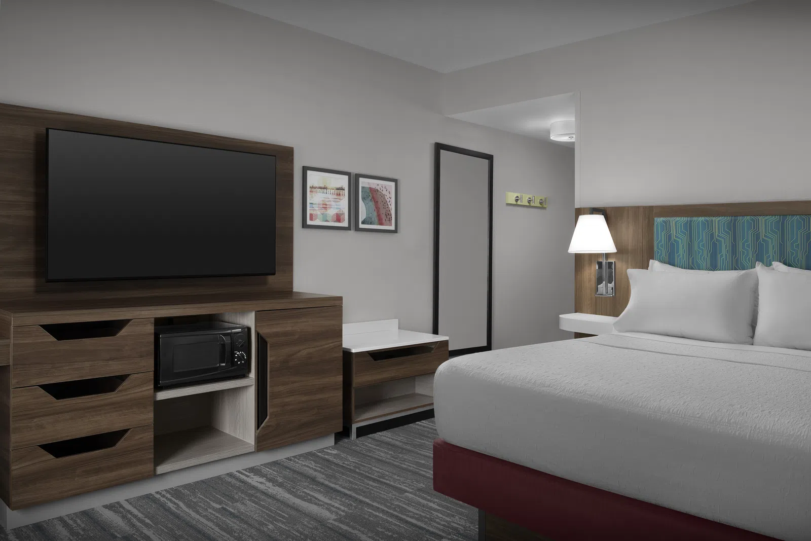 Modern hotel room with a large bed, wall-mounted TV, wooden furniture, microwave, and framed artwork on the wall.
