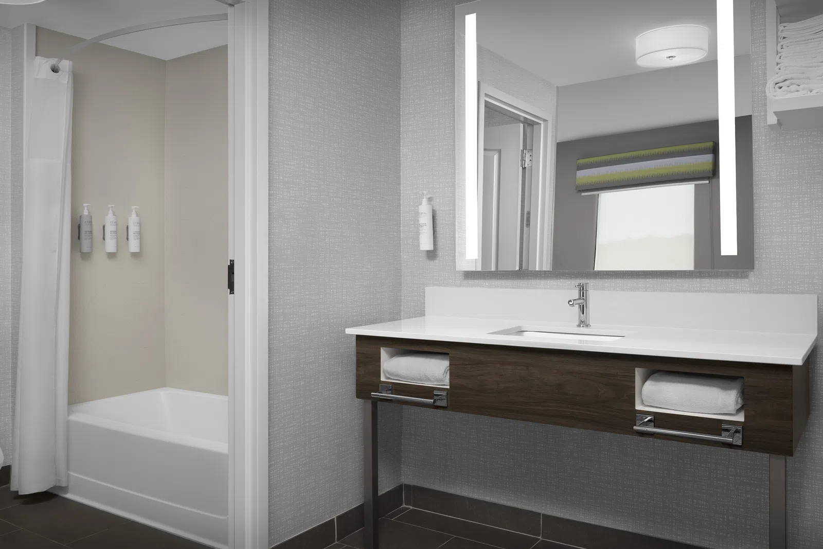 Modern bathroom with floating wooden vanity, large mirror, bathtub, and gray textured walls.