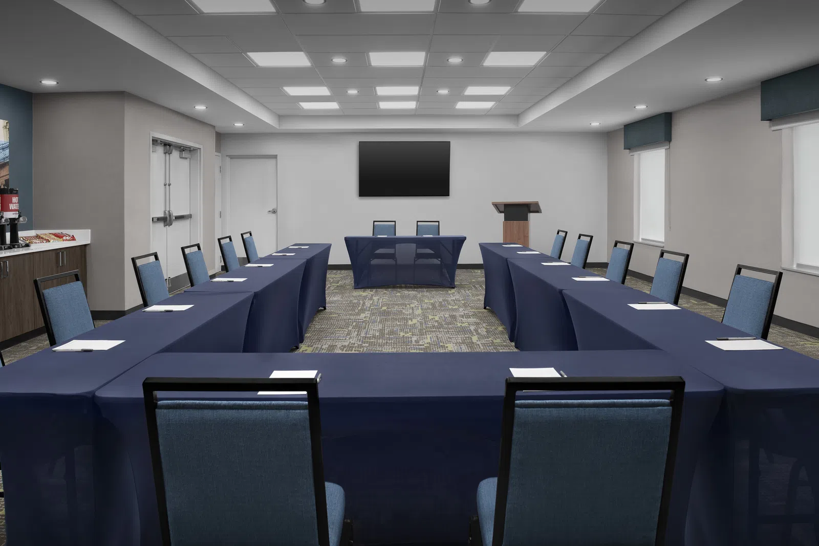 Modern U-shaped conference room with navy table covers, blue chairs, podium, and large screen on white wall.