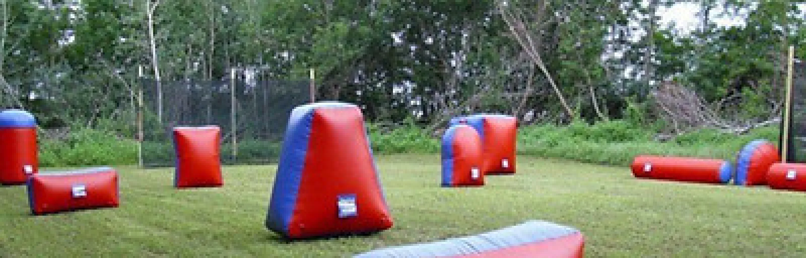 Inflatable red and blue paintball bunkers set up on grassy field with trees in the background for outdoor game.