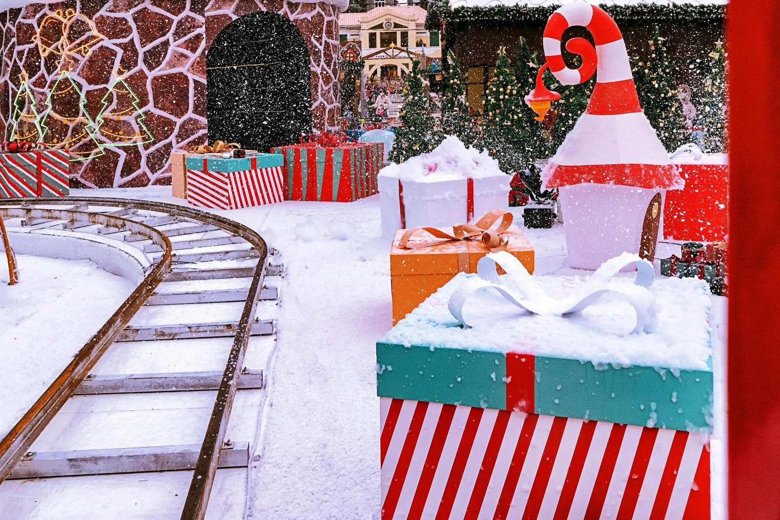 Festive holiday scene with large wrapped gifts, snow-covered ground, Christmas trees, and a toy train track.