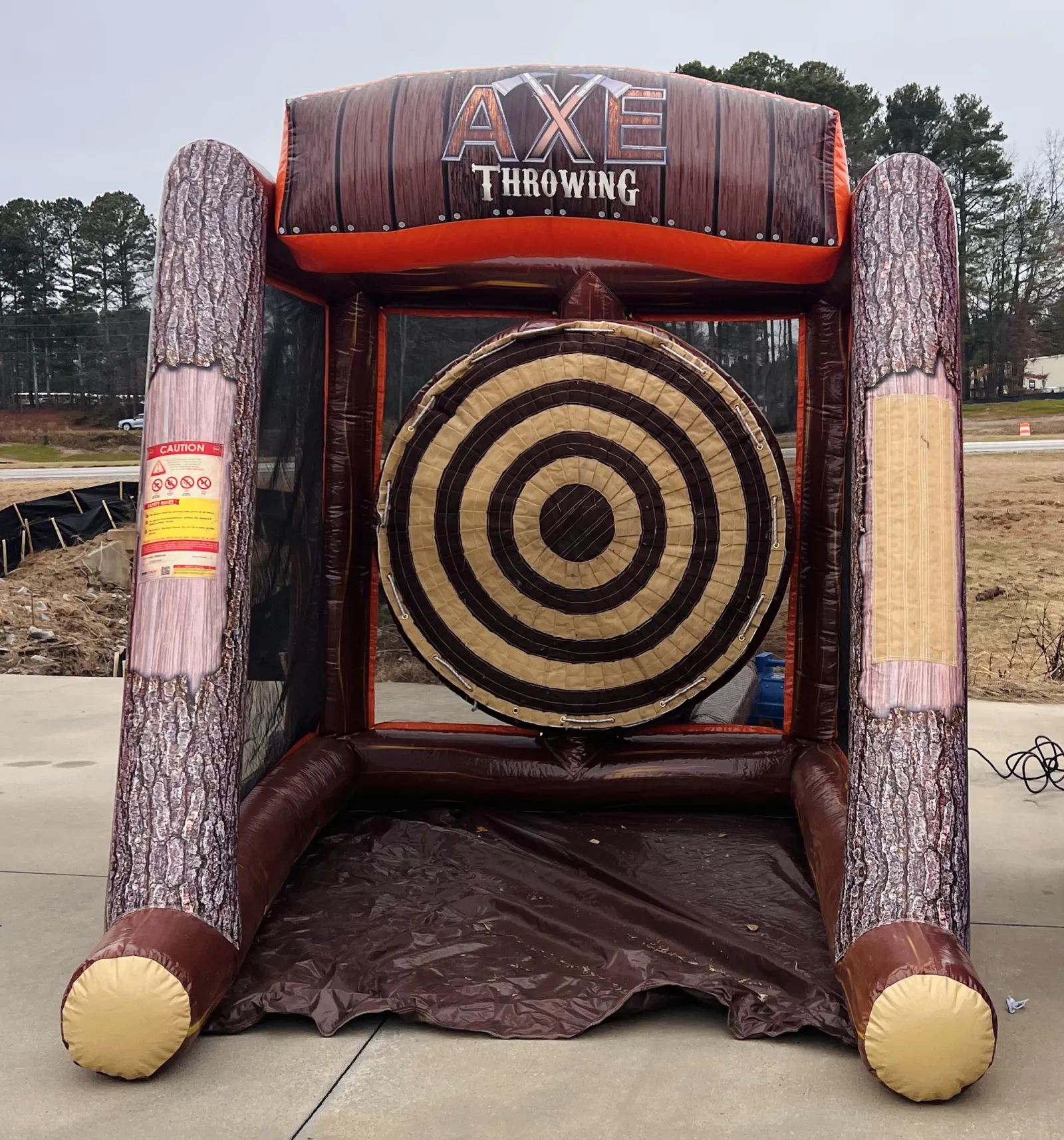 Inflatable axe throwing game with large target and wood log design set up outdoors on concrete.