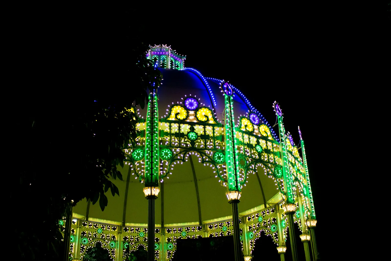 Illuminated gazebo decorated with vibrant green, yellow, and purple lights glowing brightly at night.
