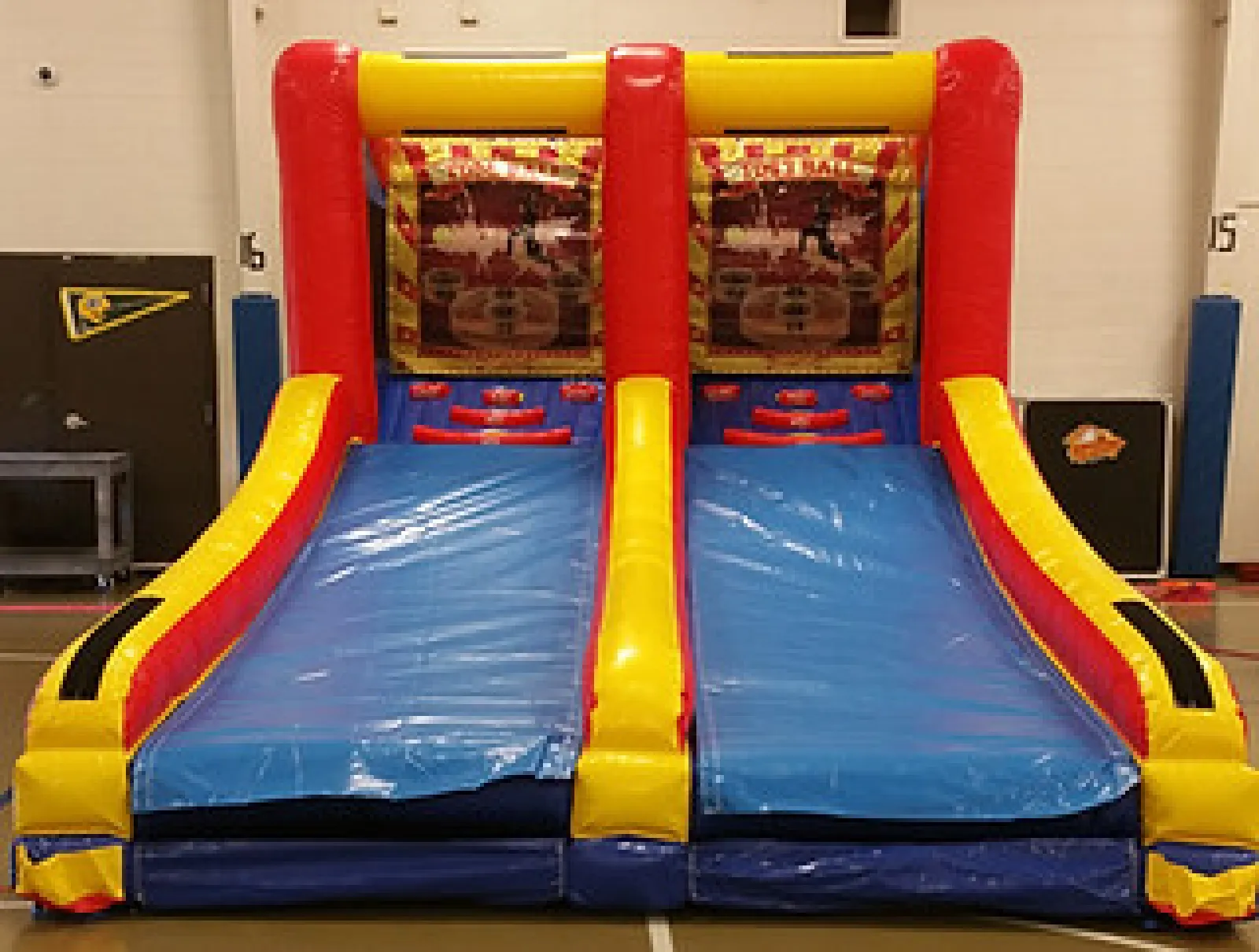 Inflatable basketball shooting game with two blue lanes and red and yellow borders set indoors.