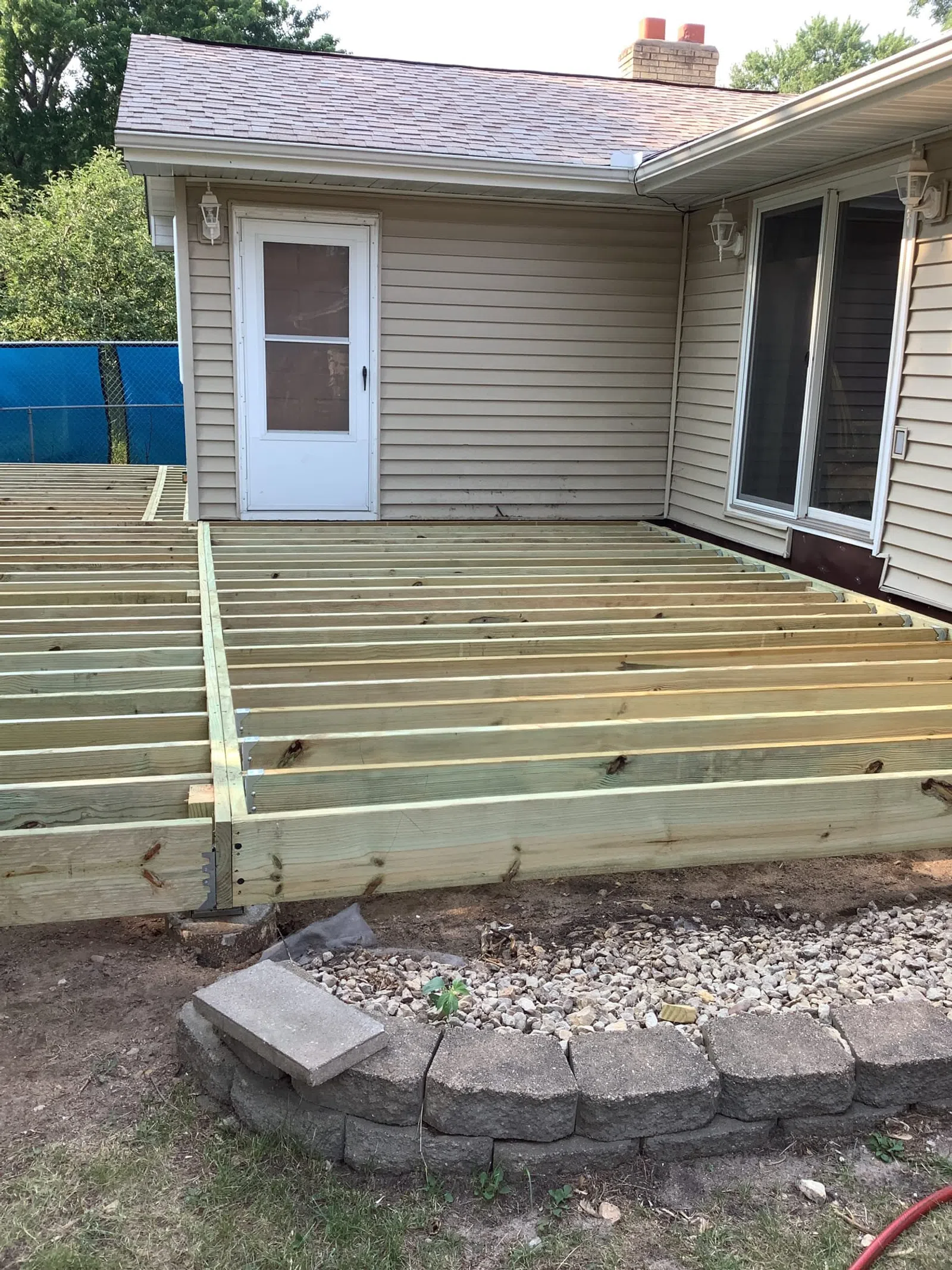 Wooden deck frame construction attached to a beige house with sliding glass door and white back door