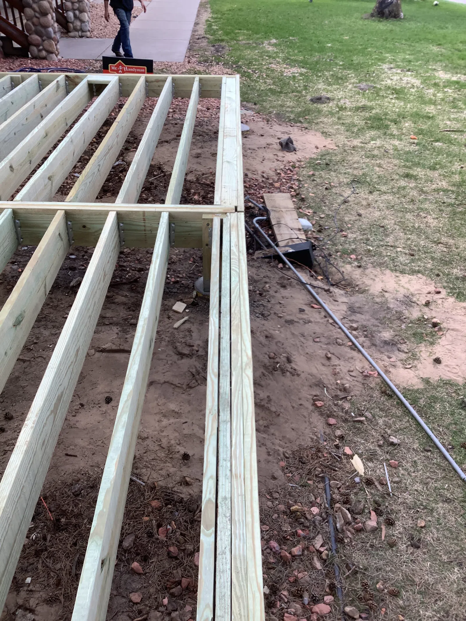 Wooden deck frame construction in progress on a backyard with grass and a walkway visible.