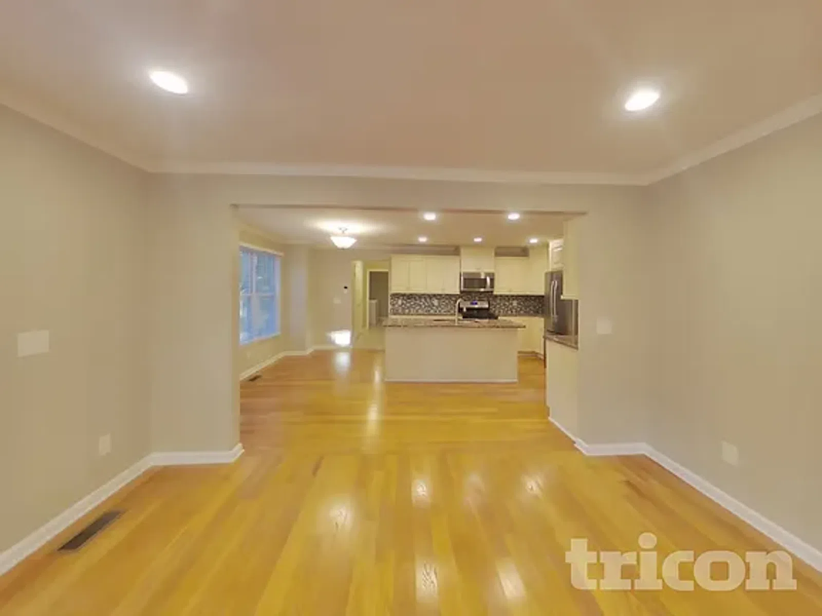 Spacious open floor plan with hardwood floors, beige walls, and modern kitchen with island and mosaic backsplash.
