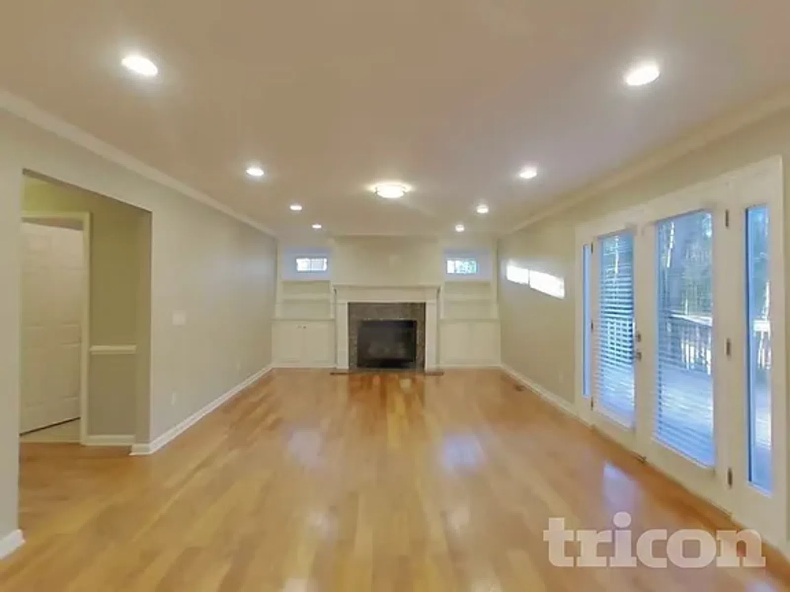 Spacious empty living room with hardwood floors, fireplace, built-in shelves, and large windows with glass doors.
