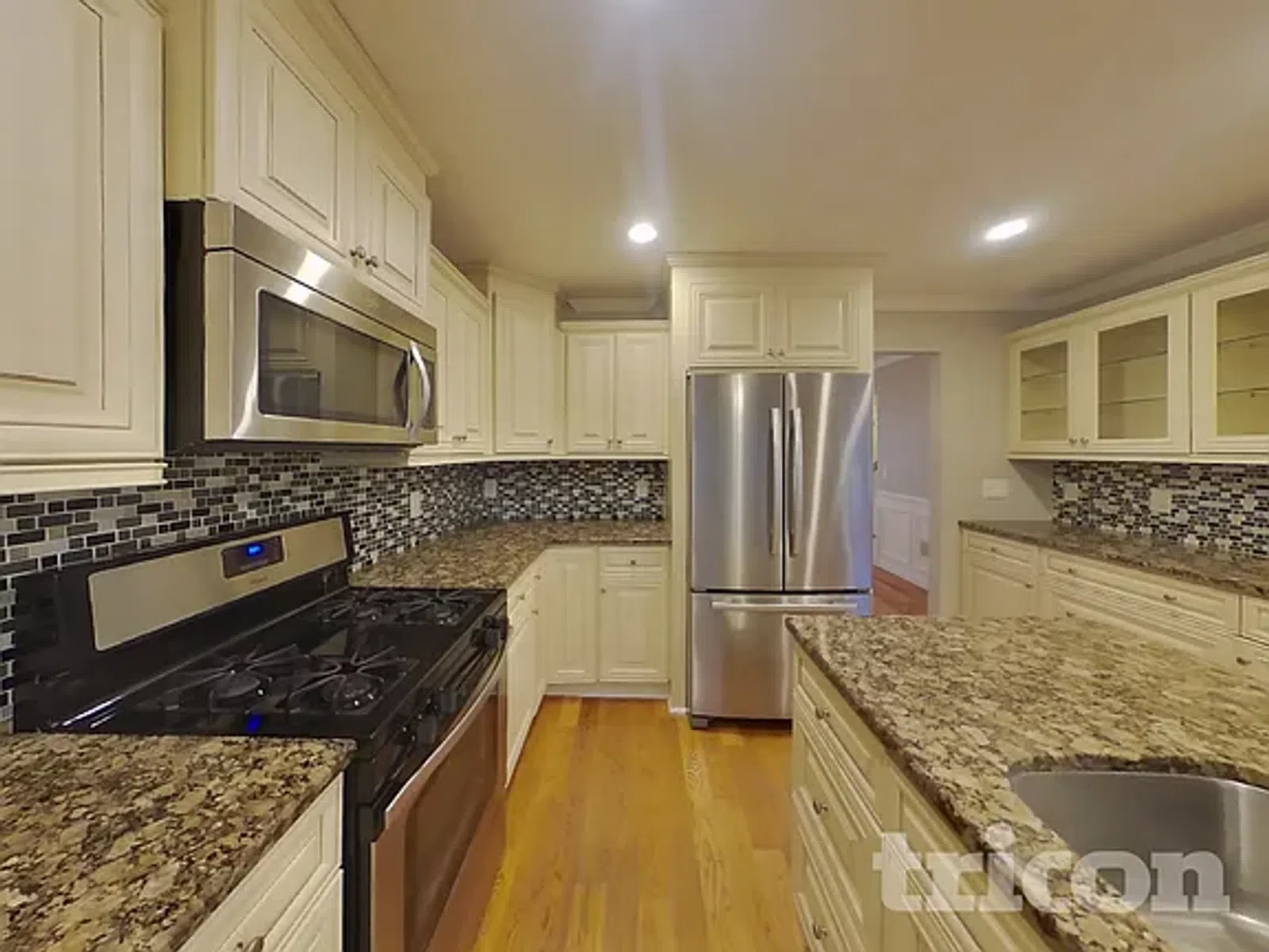 Modern kitchen with stainless steel appliances, granite countertops, mosaic tile backsplash, and cream cabinetry.