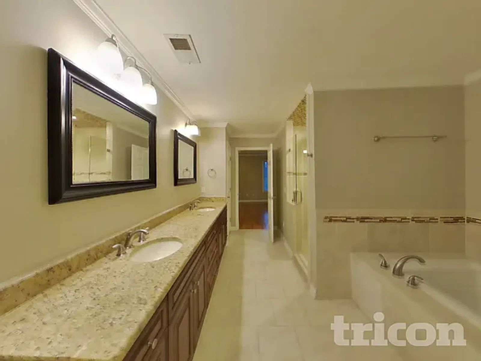 Spacious bathroom with granite double vanity, framed mirrors, shower, and bathtub with tile accents.