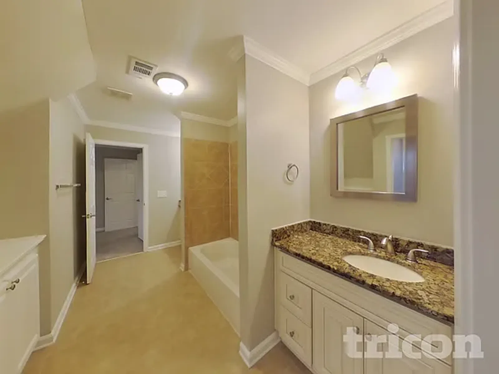 Spacious bathroom with granite countertop vanity, bathtub with tiled wall, and beige walls and flooring.