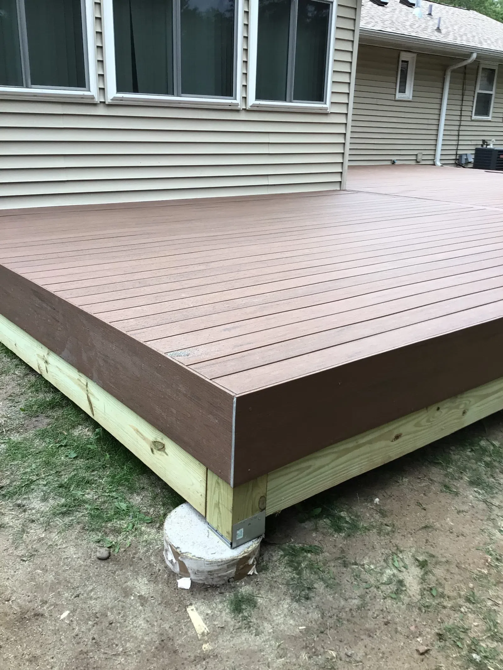Newly constructed wooden deck with composite brown decking boards next to a beige house exterior.