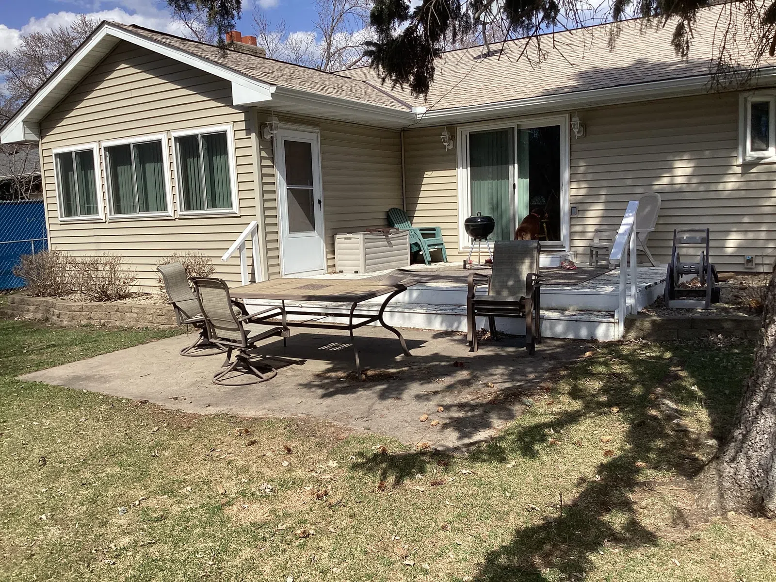 Backyard patio with outdoor table, chairs, grill, and beige siding house under a clear sky.