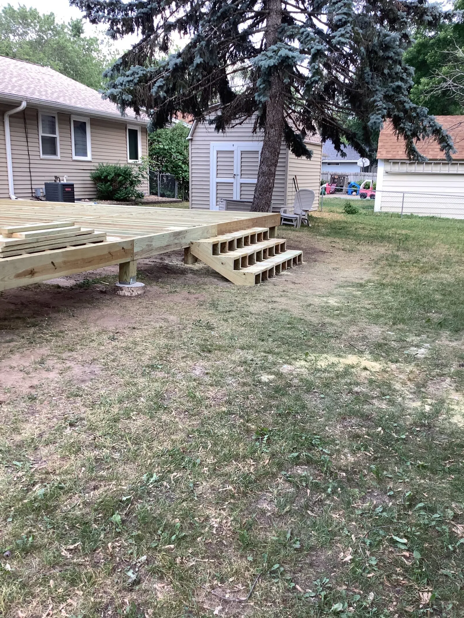 Partially constructed wooden deck with steps in a backyard near houses and a large tree
