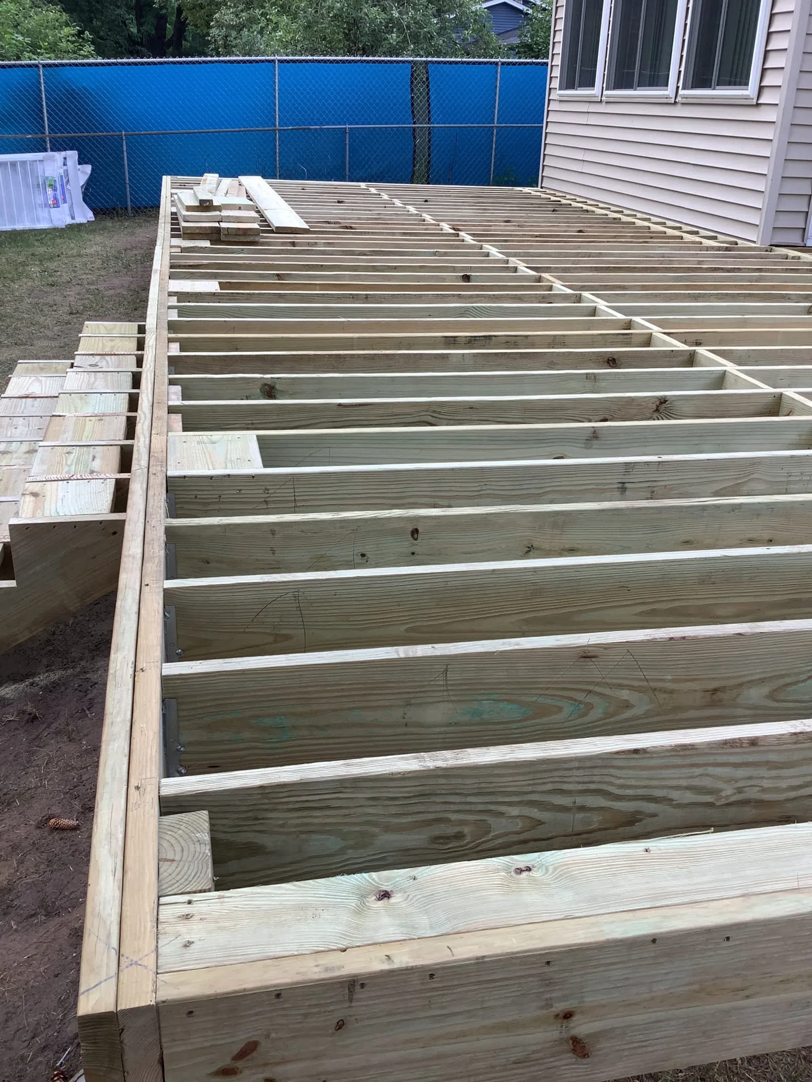 Wooden deck frame construction next to house with visible joists and stairs framed in backyard.
